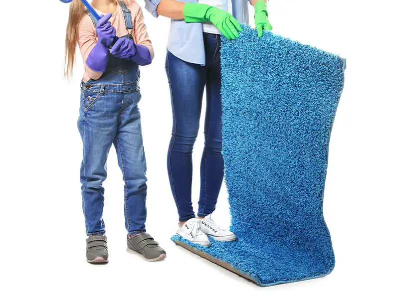 A little girl is using a carpet beater to clean the carpet